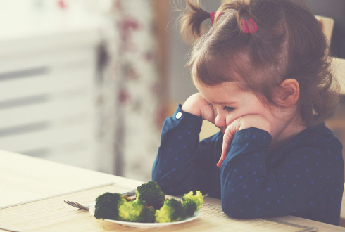 Foto di una bambina seduta a tavola che non vuole mangiare