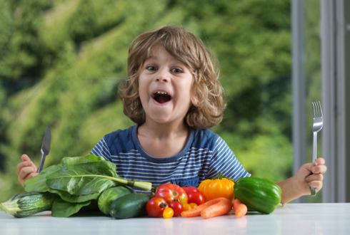 Bambino seduto a tavola felice di mangiare le verdure