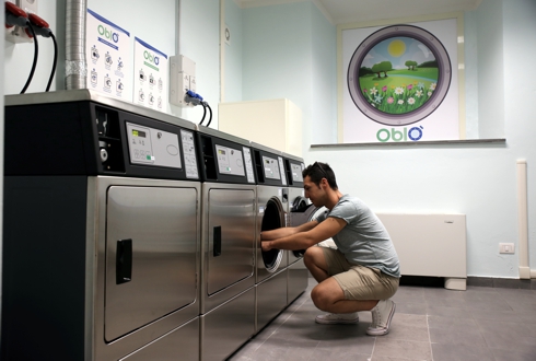 Foto lavanderia Oblò, ragazzo davanti ad una lavatrice che mette il bucato